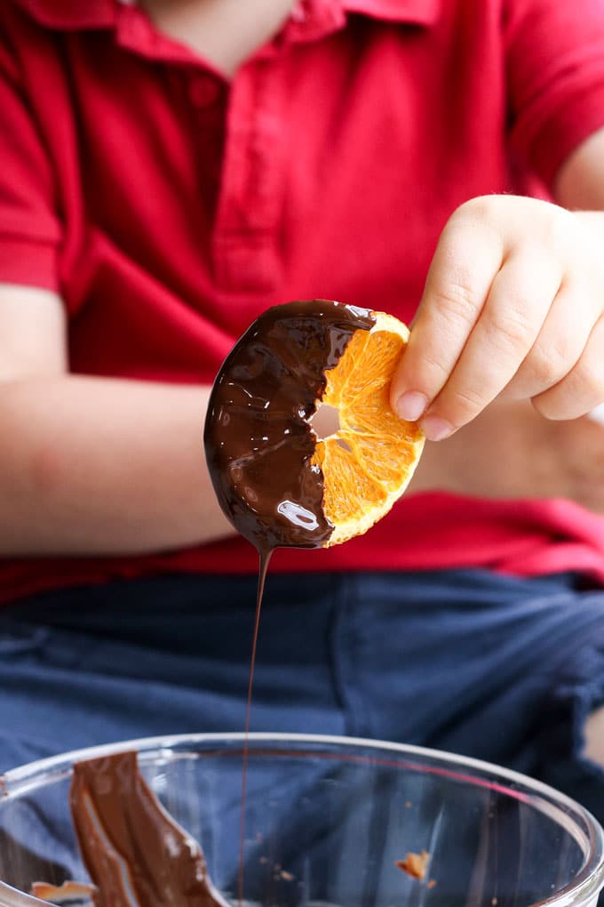 Child Dipping Dried Oranges into Chocolate