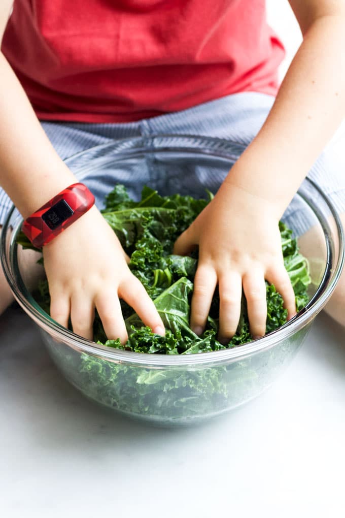 Child Massaging Kale in Bowl with Olive Oil.