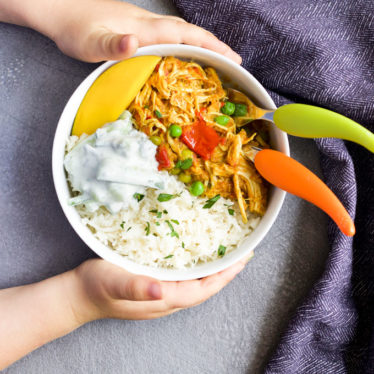 Child Grabbing Bowl of Chicken Curry and Rice Topped with Mango and Cucumber Riata