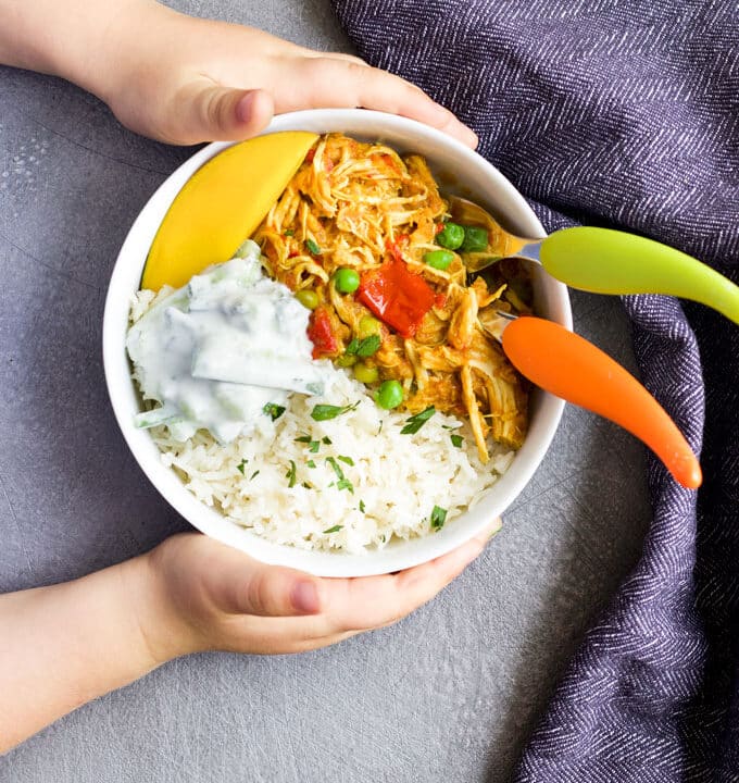 Child Grabbing Bowl of Chicken Curry and Rice Topped with Mango and Cucumber Riata