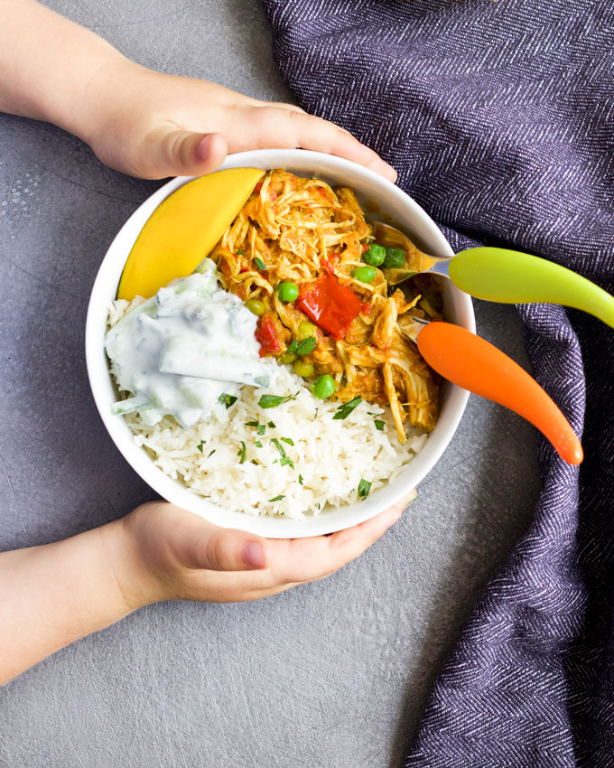 Child Grabbing Bowl of Chicken Curry and Rice Topped with Mango and Cucumber Riata