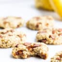 Close Up Side Shot of Banana Oatmeal Cookie with Bite Removed. Banana Oat Cookies and Bananas in Background.