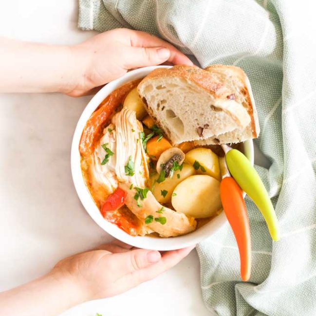 Child Holding Bowl of Slow Cooker Chicken Casserole Served with Crusty Bread