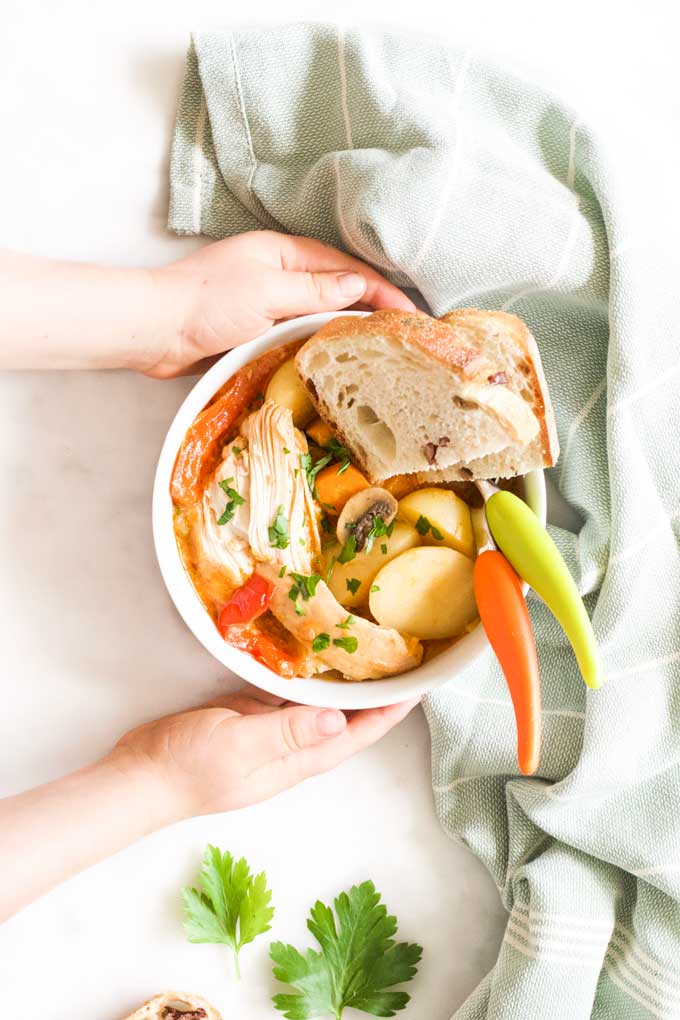 Child Holding Bowl of Slow Cooker Chicken Casserole Served with Crusty Bread