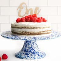 First Birthday Cake on Blue Cake Stand Topped with Raspberries and a "One" Cake Topper.