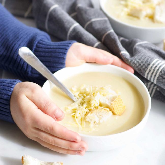 Child Holding Bowl of Cauliflower Cheese Soup