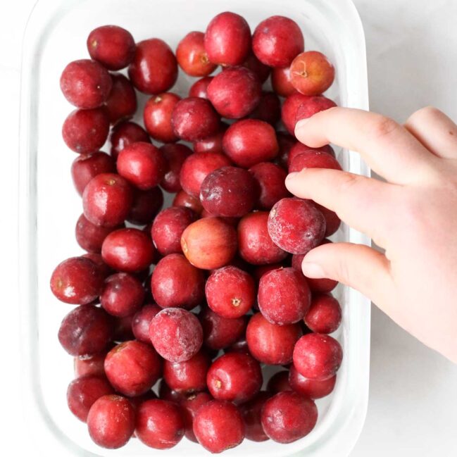 Child's Hand Reaching in to Take a Frozen Grape from Container