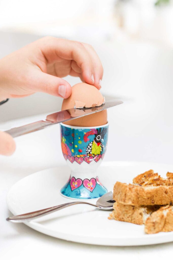 Child Cutting Top off Egg in Egg Cup (From a Plate of Egg and Soldiers)