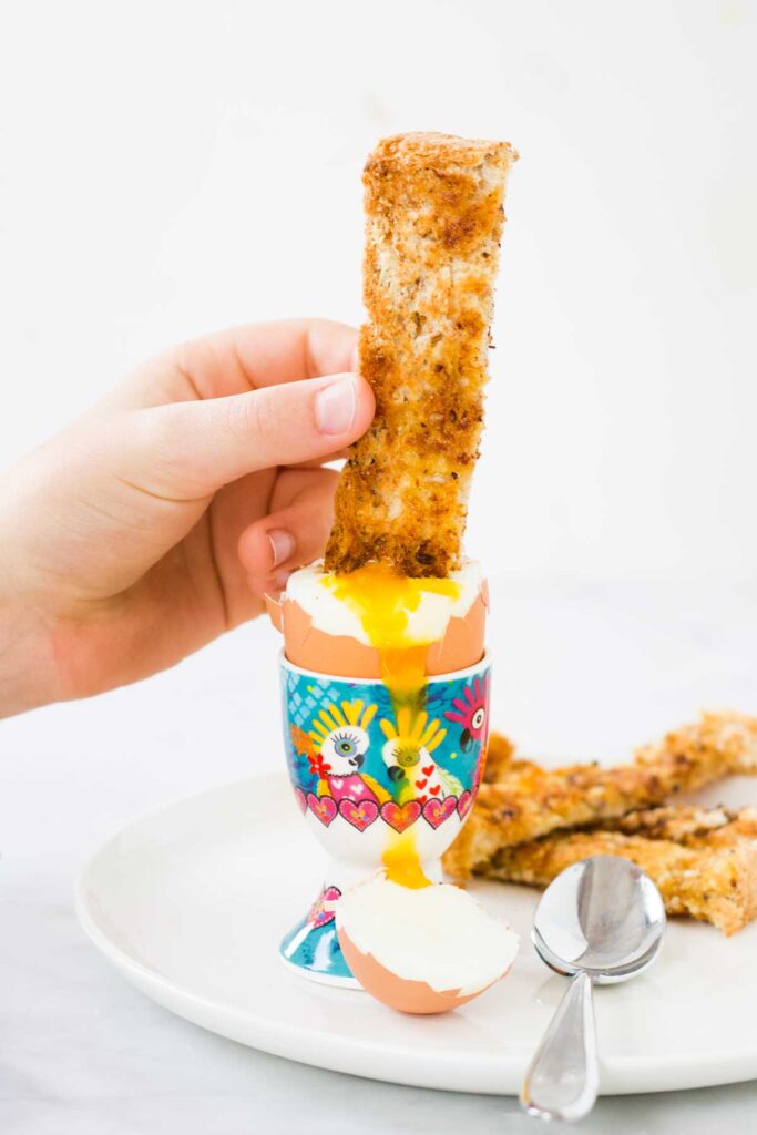 Child Dipping Toast Soldier into Yolk of Dippy Egg