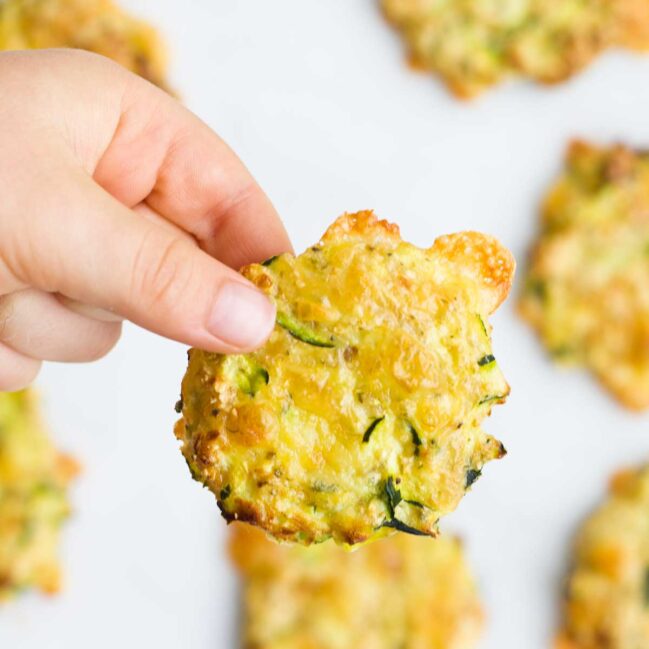 Child's Hand Holding Up a Zucchini Bite to the Camera