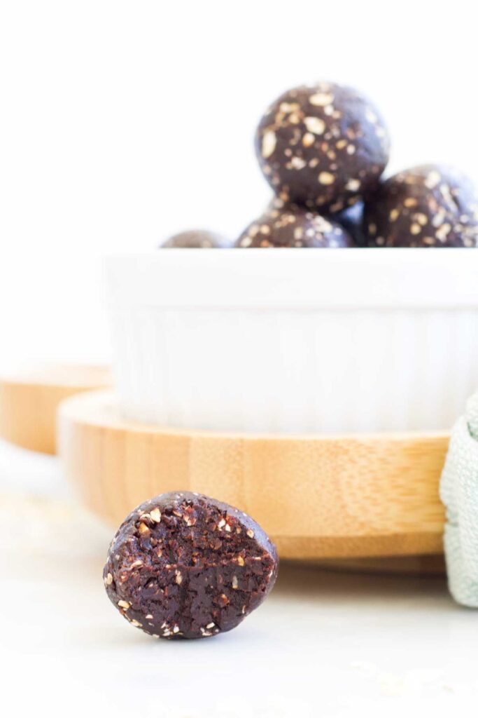 Side Shot of Cocoa Energy Balls in White Bowl. Focus on One Ball with Bite Removed Sitting In Front of Bowl