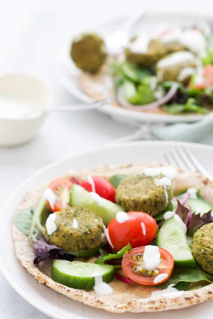 Two Plates of Falafel on Pita Bread with Salad and Yogurt Dressing