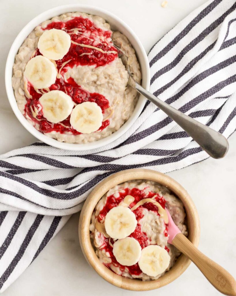 Adult and Toddler Bowl of Banana Porridge Topped with Crushed Raspberries and Banana Slices