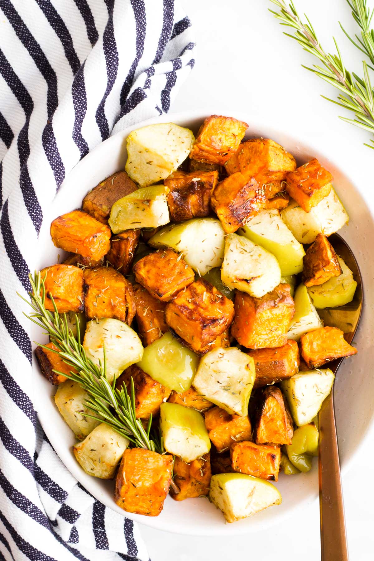 Over head Shot of a Serving Bowl of Roasted Sweet Potato and Apple with Striped Napkin and Sprig of Rosemary in Background 