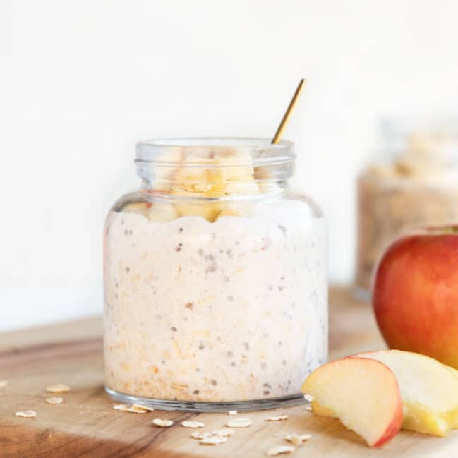 Jar of Apple Overnight Oats on Wooden Board with and Apple and Slices of Apple Scattered Next to it.