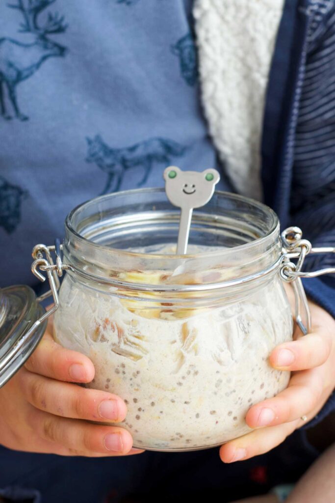 Side on Shot of Child Holding Glass Jar of Overnight Oats with Teddy Spoon
