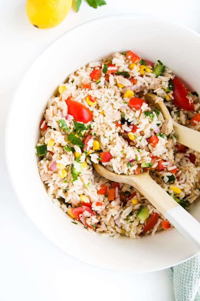 Top Down Shot of Tuna Rice Salad in Large White Bowl with Wooden Salad Spoons. Lemon in Background