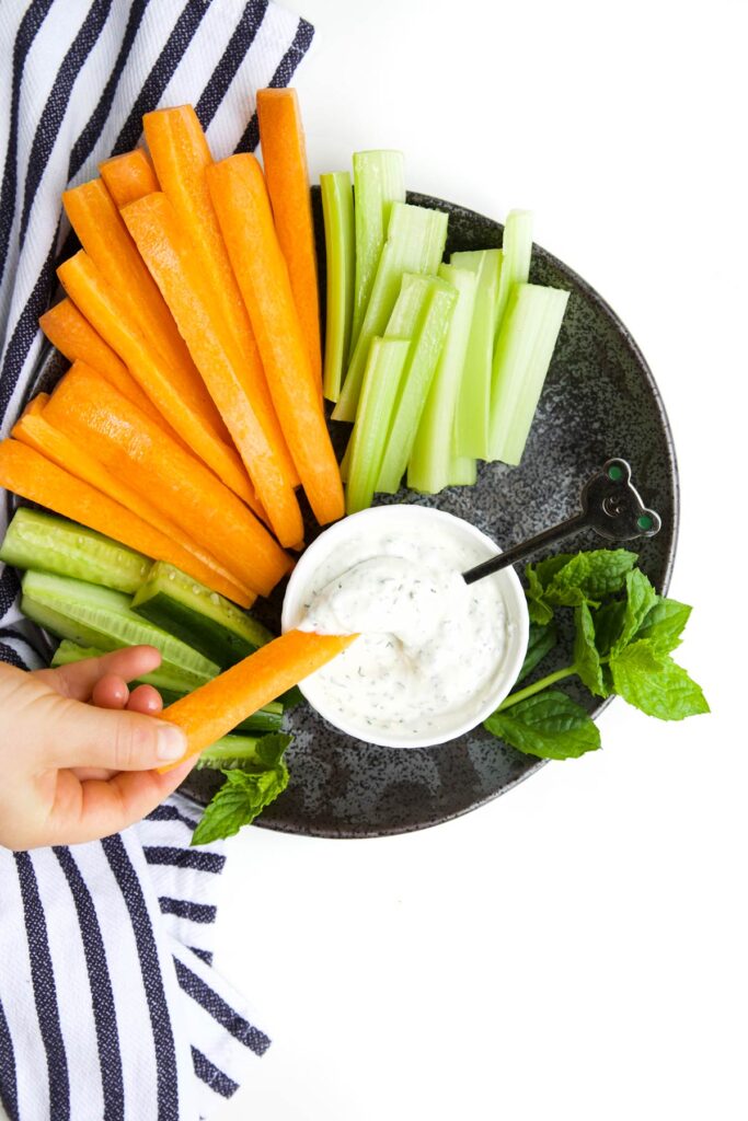 Child Dipping a Carrot Stick into Bowl of Mint Yogurt Dip