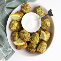 Broccoli Tots in White Bowl with Lemon Yogurt Dip and slices of Lemon