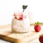 A jar of Strawberry Overnight Oats Sitting on Wooden Board with Strawberries and Oats Scattered