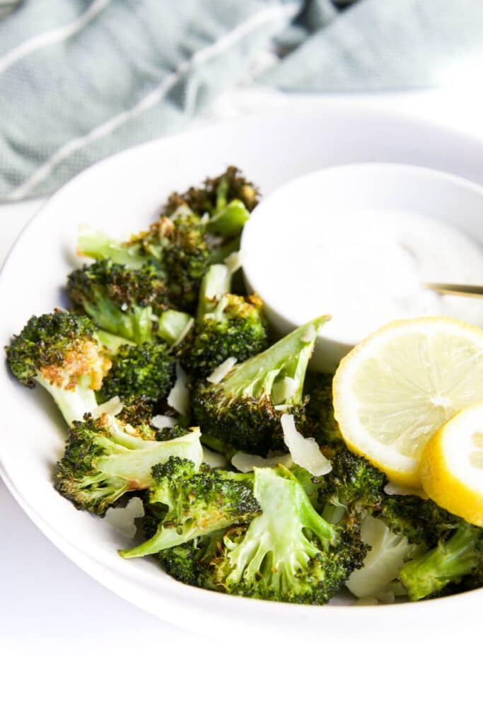 Side Shot of Air Fried Broccoli in Bowl Served with Yogurt Dip and Lemon Slices