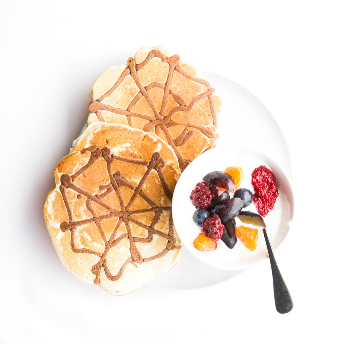 Plate of 2 Spider Web Pancakes with a Side of Yogurt and Fruit