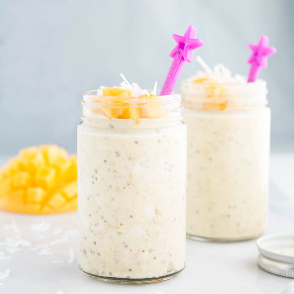 Side Shot 2 Glass Jars of Mango Overnight Oats Topped with Mango and Coconut With Pink Star Spoon