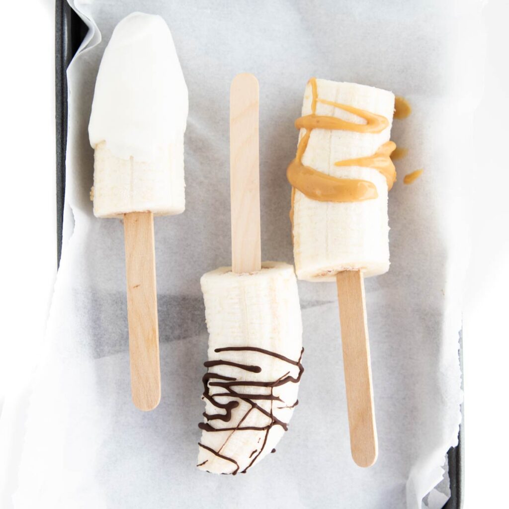 Flat Lay of Frozen Bananas One Dipped in Yogurt, One Drizzled with Chocolate One Drizzled with Peanut Butter