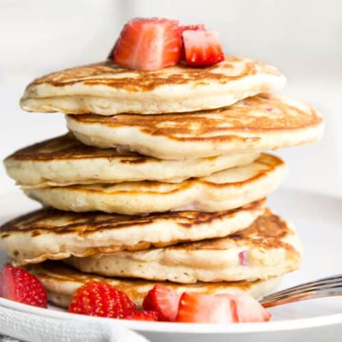 Side Shot of a Strawberry Pancake Stack With Chopped Strawberries on Top and Side of Plate