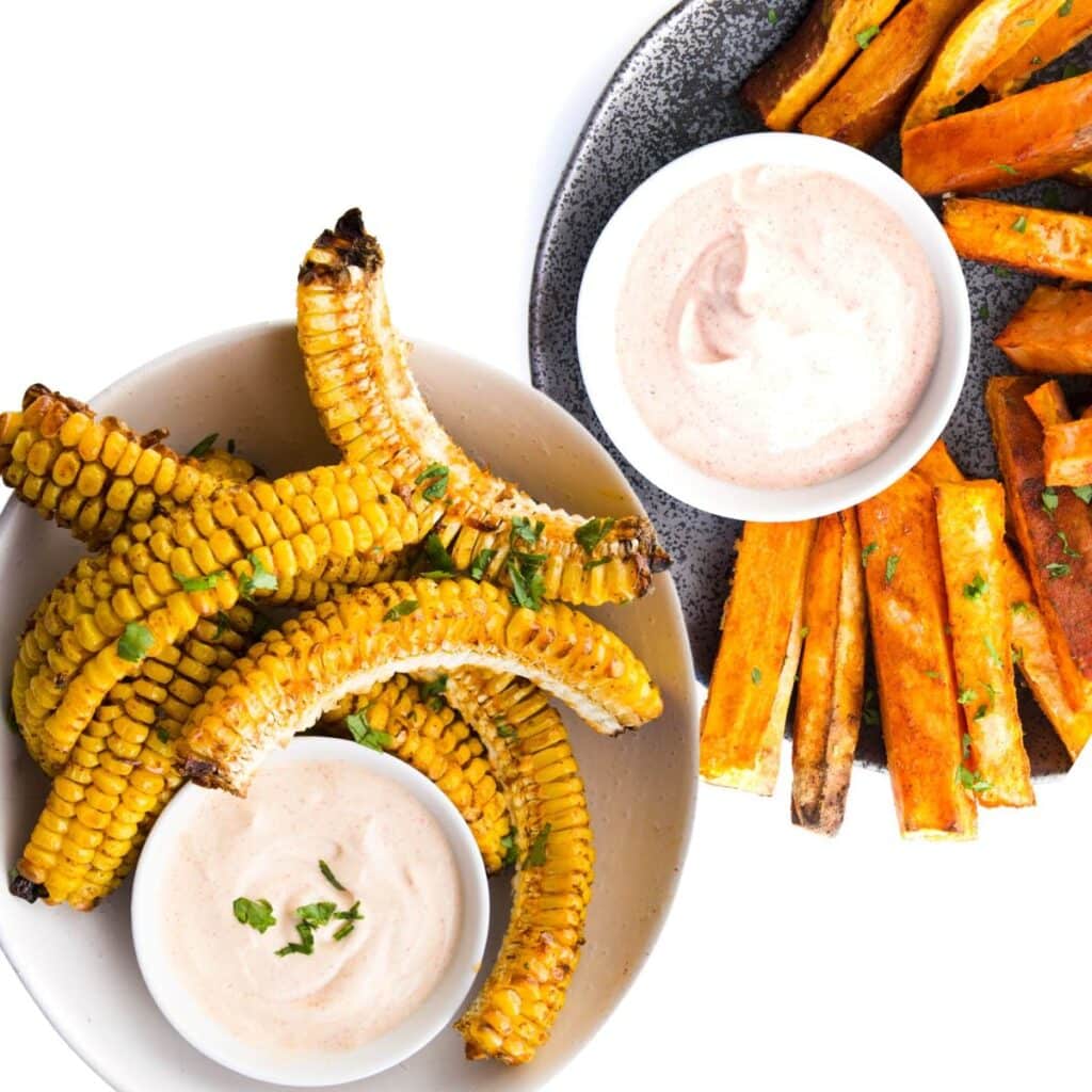 Top Down of Two Plates One With Corn Ribs and Sweet Paprika Dip the Second with Sweet Potato Wedges adn Smoked Paprika Dip