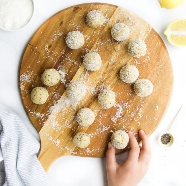 Lemon Bliss Balls on Round Wooden Board, Hand Reaching Out to Grab Ball.