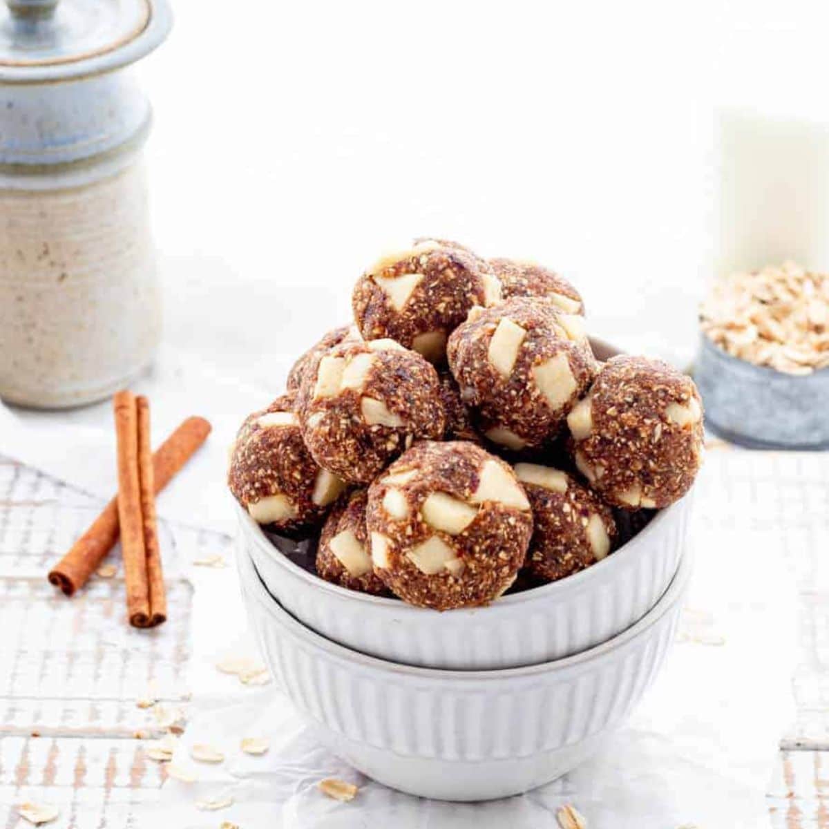 Apple Pie Energy Balls Sitting in White Bowl With Ingredients in Background. 