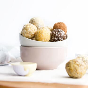 A Selection of Different Flavoured Nut Free Bliss Balls in Bowl with Balls Scattered in Background.